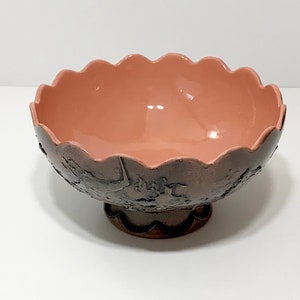 May include: A pink ceramic bowl with a scalloped rim and a raised base. The bowl has a textured, embossed design on the exterior.