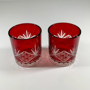 May include: Two red glass tumblers with a white etched geometric design. The glasses are clear and have a rounded bottom.