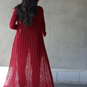 May include: A long, red, open-front cardigan with a loose, flowing fit. The cardigan is made of a soft, textured knit fabric.