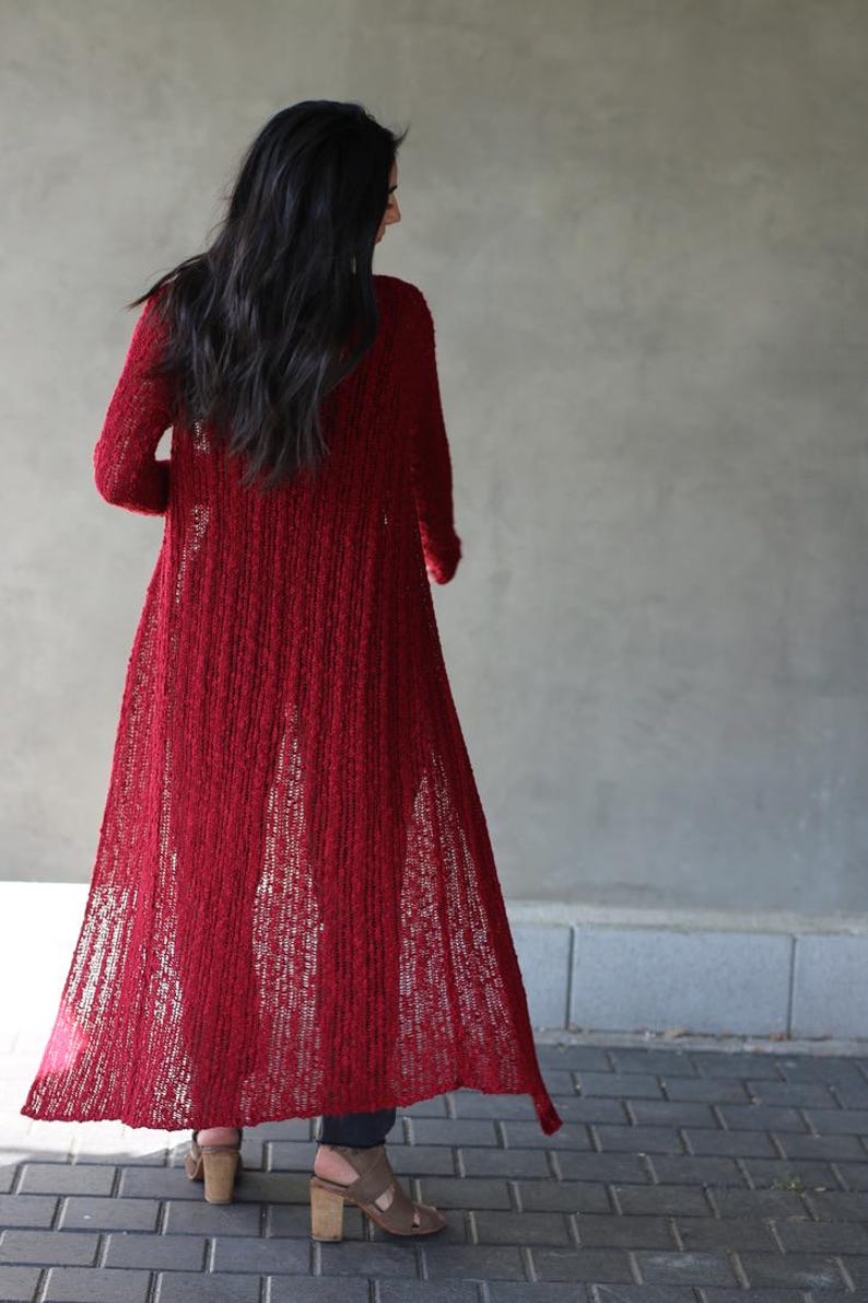May include: A long, red, open-front cardigan with a loose, flowing fit. The cardigan is made of a soft, textured knit fabric.
