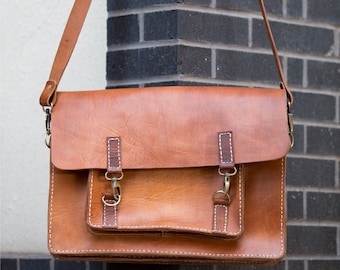 May include: A brown leather satchel bag with two adjustable straps and a flap closure. The bag has a front pocket and a main compartment.