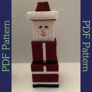 May include: A three-dimensional Santa Claus figure made of plastic canvas. The figure is stacked in three blocks, with the top block being the head, the middle block being the body, and the bottom block being the legs. The figure is red and white with black accents. The figure is a craft project and is not finished. The text "Krafts by Kruger" is visible in the upper right corner of the image.