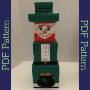 May include: A green, white, and red plastic canvas pattern of a leprechaun holding a pot of gold. The pattern is made up of four stacked boxes. The leprechaun is wearing a green hat, a green jacket, and a white shirt. The pot of gold is black with a gold coin and a shamrock.