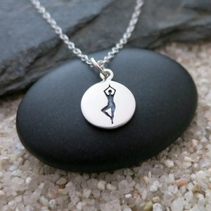 May include: A silver necklace with a round pendant featuring a cutout silhouette of a person in a yoga pose.