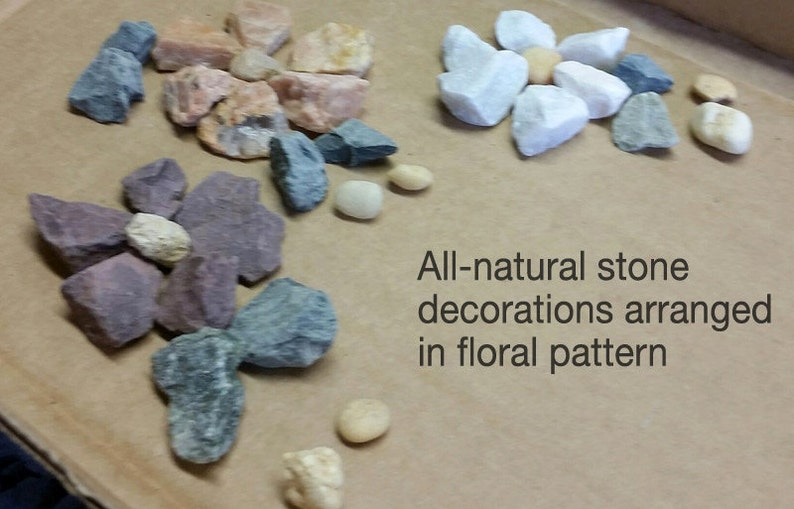 May include: Arrangement of natural stones in various colors, including gray, pink, and white, displayed in a floral pattern. The image includes the text "All-natural stone decorations arranged in floral pattern."