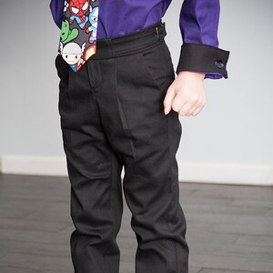 Puede incluir: Un joven que lleva pantalones negros con una camisa morada y una corbata colorida. Lleva zapatillas negras y blancas con un estampado tie-dye colorido.