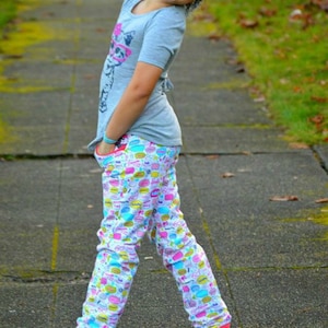 May include: A young person wearing a grey t-shirt with a graphic print and colourful patterned trousers. The trousers have a pink, blue, yellow, and white design with various shapes and words.