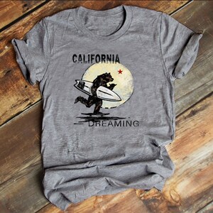 May include: Gray t-shirt with a vintage-style graphic of a bear surfing with the text "CALIFORNIA DREAMING" and a red star.