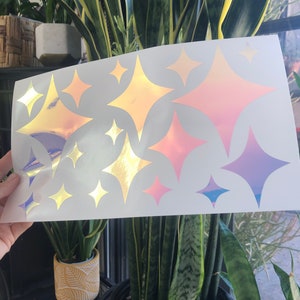 Puede incluir: Una hoja de pegatinas de vinilo iridiscente con 12 estrellas en forma de diamante en varios tonos de rosa, morado y dorado. Las pegatinas son perfectas para agregar un toque de brillo a cualquier proyecto.