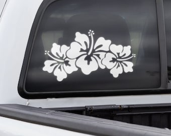 Może przedstawiać: Biały pick-up z czarną skrzynią ładunkową i białą naklejką z kwiatem hibiskusa na tylnej szybie.
