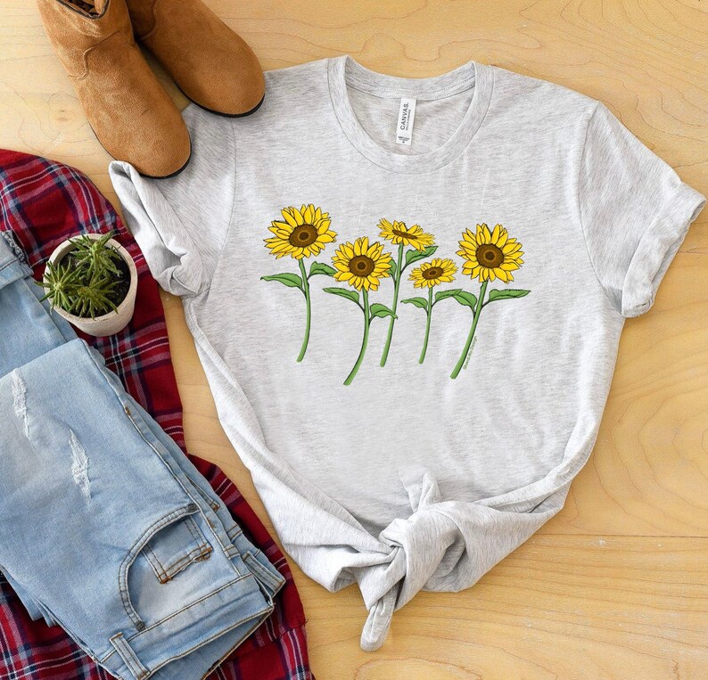 K&ouml;nnte beinhalten: Ein graues T-Shirt mit einem Aufdruck von f&uuml;nf gelben Sonnenblumen mit gr&uuml;nen Stielen und Bl&auml;ttern.
