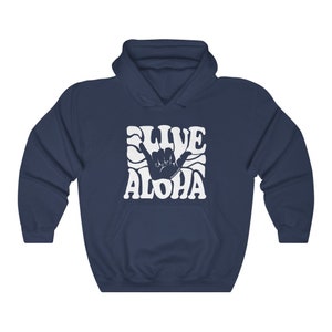 May include: A navy blue hoodie with a white graphic of a hand making the shaka sign with the text "Live Aloha" in a retro font.