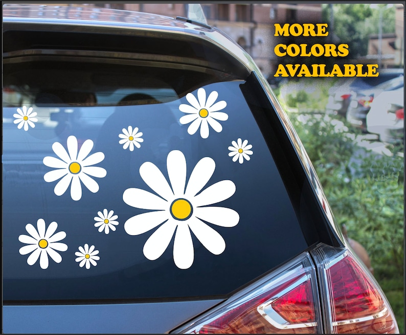 May include: A car window with a decal of white daisies with yellow centers. The text "MORE COLORS AVAILABLE" is in yellow letters on the car.