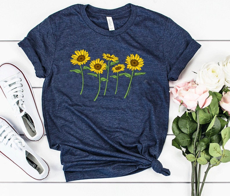 K&ouml;nnte beinhalten: Ein marineblaues T-Shirt mit einem Aufdruck von f&uuml;nf gelben Sonnenblumen auf Stielen. Das Shirt ist aus einem weichen, bequemen Material.