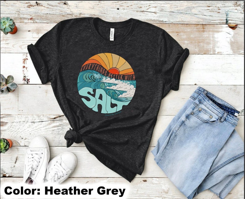 Puede incluir: Camiseta gris jaspeada con un gr&aacute;fico de una puesta de sol sobre olas oce&aacute;nicas y el texto "Everything's Better With Salt".