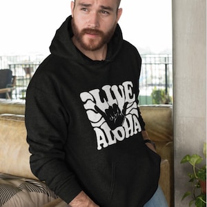 May include: A black hooded sweatshirt with a white graphic print of a hand making the shaka sign with the text "Live Aloha" in a retro font.