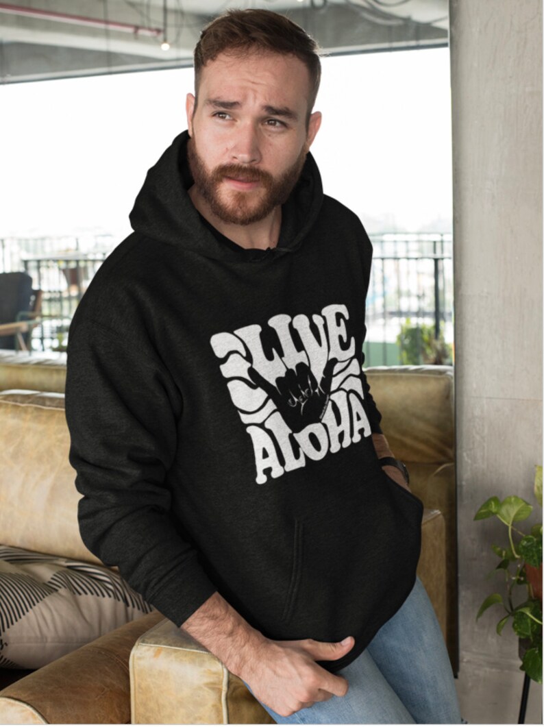 May include: A black hooded sweatshirt with a white graphic print of a hand making the shaka sign with the text "Live Aloha" in a retro font.