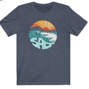 Puede incluir: Una camiseta azul con un gr&aacute;fico retro de una puesta de sol sobre olas oce&aacute;nicas. El gr&aacute;fico dice "Everything's Better With Salt".