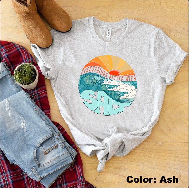 Puede incluir: Una camiseta gris con un gr&aacute;fico retro de olas y un sol. El gr&aacute;fico dice "Everything's Better With Salt".
