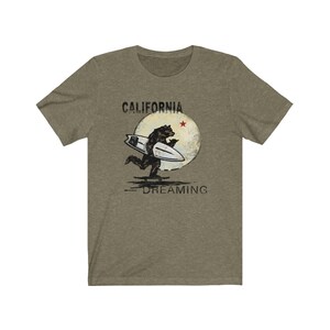 May include: A green t-shirt with a graphic of a bear surfing on a wave with a moon and a red star in the background. The text "CALIFORNIA DREAMING" is printed below the graphic.
