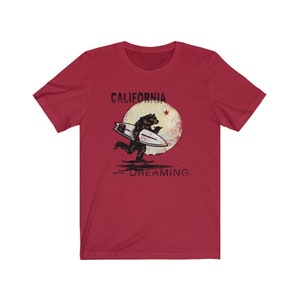 May include: Red t-shirt with a graphic of a bear surfing on a wave with a red star and the text "CALIFORNIA DREAMING" printed on it.