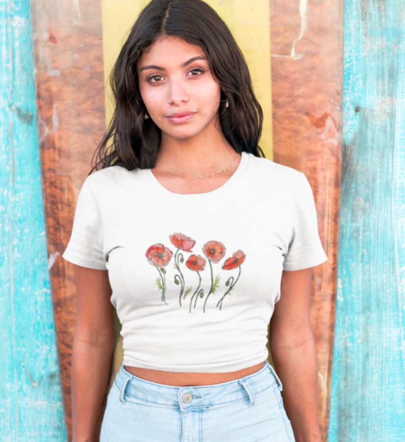 K&ouml;nnte beinhalten: Ein wei&szlig;es, bauchfreies T-Shirt mit einem Aufdruck von roten Mohnblumen auf der Vorderseite.