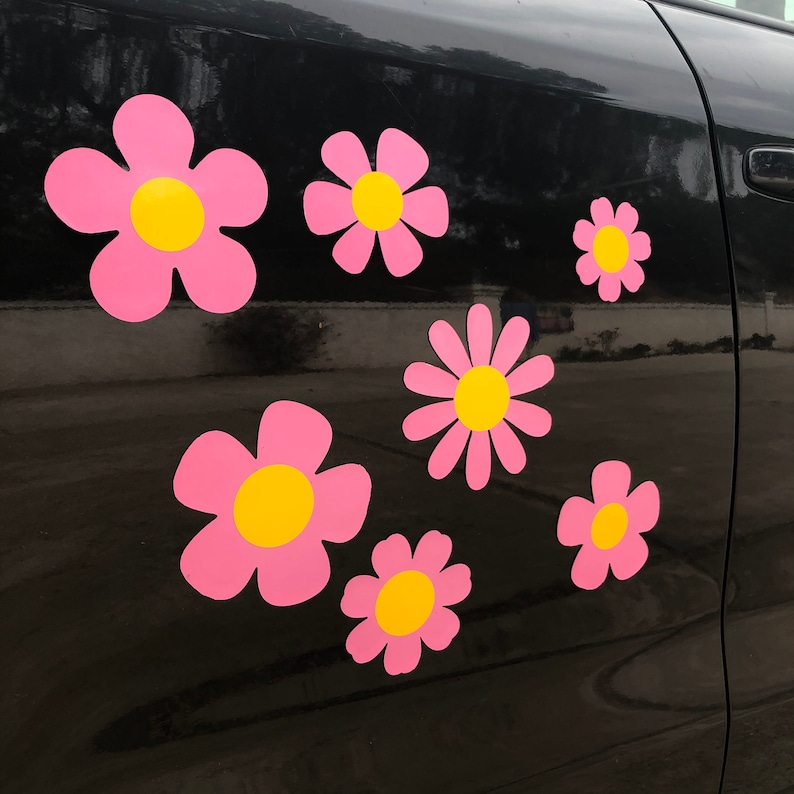 May include: A black car with pink flower decals on the side. The flowers have yellow centers and are arranged in a random pattern.