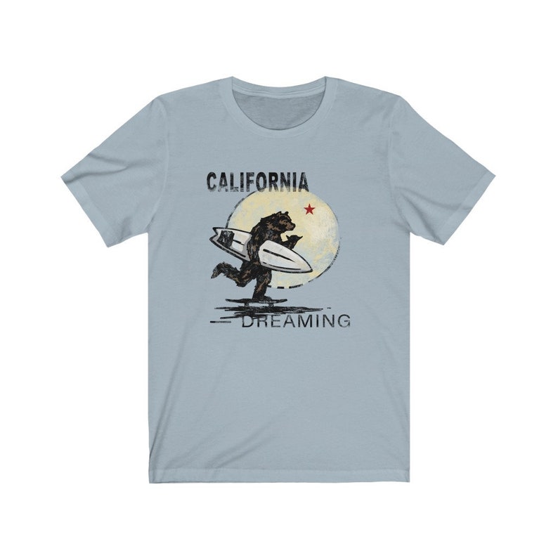 May include: A light blue t-shirt with a graphic of a bear surfing on a wave with a red star and the text "CALIFORNIA DREAMING".