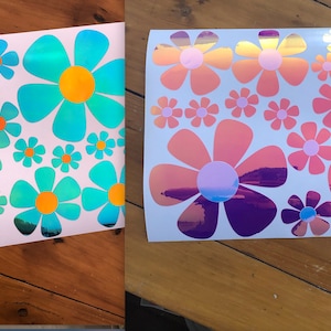May include: Two sheets of white paper with iridescent flower stickers. The stickers are in various sizes and feature a rainbow effect. The flowers are in shades of blue, pink, and purple.