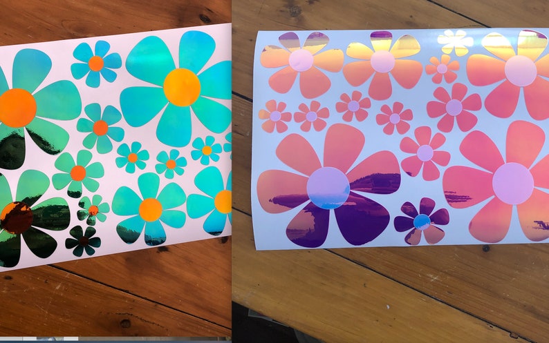 May include: Two sheets of white paper with iridescent flower stickers. The stickers are in various sizes and feature a rainbow effect. The flowers are in shades of blue, pink, and purple.