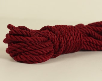 May include: A roll of thick, dark red cotton rope. The rope is coiled and tied in a knot.