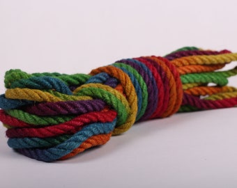 May include: A bundle of colorful rope in a rainbow of hues, including red, orange, yellow, green, blue, and purple. The rope is tightly coiled, showcasing its textured, twisted fibers. This decorative rope is suitable for various craft projects.