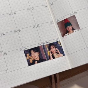 May include: A planner with a grid layout, featuring small photos of people and a Christmas-themed image. The planner's pages are open, displaying dates and Japanese characters. The photos are placed on specific dates.