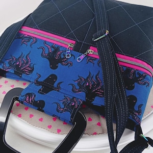 May include: A black quilted tote bag with a pink zipper and a black handle. The bag has a blue fabric lining with a pink and black octopus print.
