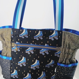 May include: A blue and gold tote bag with a roller skate pattern. The bag has a zippered pocket and two side pockets. The straps are blue and white.