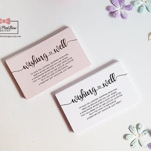 May include: Two pink and white cards with the text "wishing well" in black cursive font. The text on the cards reads "To save you looking, shopping or buying, here's an idea we hope you like trying. A honeymoon adventure is what we're after, that will bring us joy and lots of laughter. So if you wish to participate, a monetary gift would be just great."