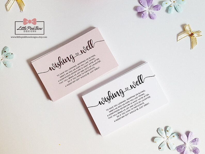 May include: Two pink and white cards with the text "wishing well" in black cursive font. The text on the cards reads "To save you looking, shopping or buying, here's an idea we hope you like trying. A honeymoon adventure is what we're after, that will bring us joy and lots of laughter. So if you wish to participate, a monetary gift would be just great."