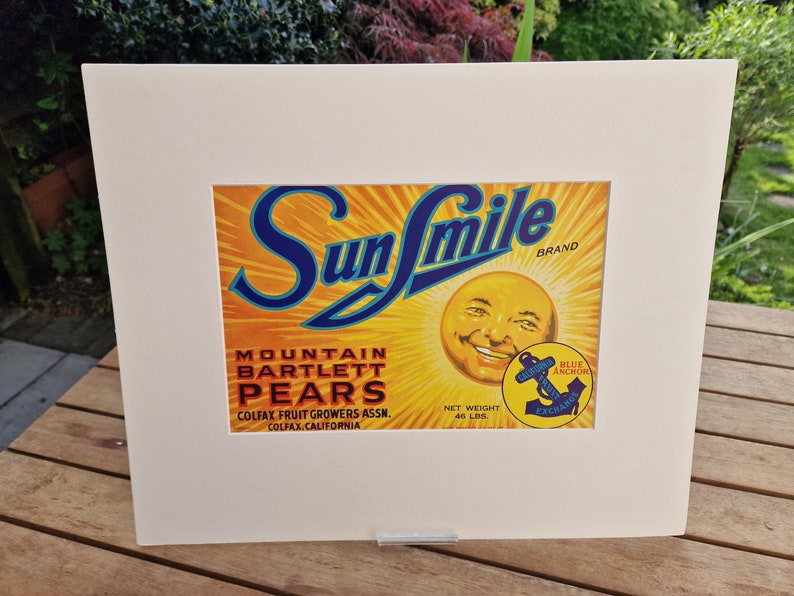 May include: Vintage Sun Smile brand label for Mountain Bartlett Pears. The label features a smiling sun with a blue anchor logo and the text "Blue Anchor Exchange".