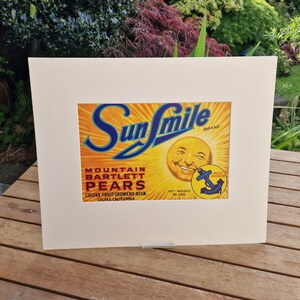 May include: Vintage Sun Smile brand label for Mountain Bartlett Pears. The label features a smiling sun face with a blue anchor logo and text that reads "Colfax Fruit Growers Assn. Colfax, California".