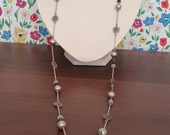 Collar largo de tono plateado con cuentas de vidrio y diseño de flor de metal.