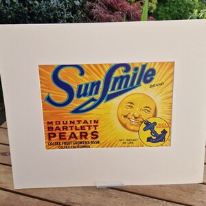 May include: A vintage Sun Smile brand label for Mountain Bartlett Pears. The label features a smiling sun face with a blue anchor logo and the text "Blue Anchor Exchange".