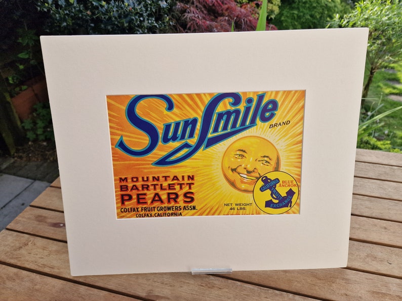 May include: A vintage Sun Smile brand label for Mountain Bartlett Pears. The label features a smiling sun face with a blue anchor logo and the text "Blue Anchor Exchange".