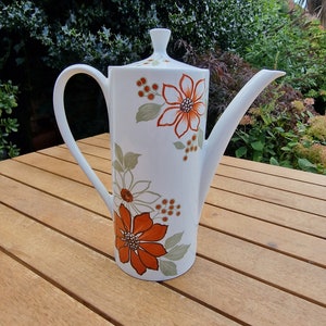 May include: White ceramic teapot with a floral design in shades of orange, green, and brown. The teapot has a lid and a spout.