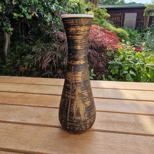 Peut inclure: Un vase en céramique noir et or avec un motif de girafe stylisé. Le vase a une surface texturée et un bord blanc.
