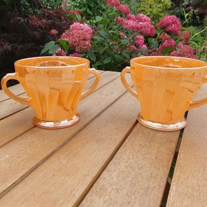 以下が含まれることがあります： 取っ手付きのオレンジ色のヴィンテージガラスカップ2個。カップはフルーテッドデザインで、真珠のような光沢があります。