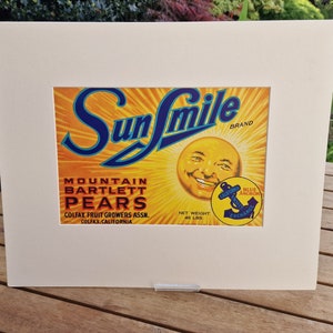 May include: Vintage Sun Smile brand label for Mountain Bartlett Pears. The label features a yellow sun with a smiling face and the text "Sun Smile" in blue lettering. The label also includes the text "Mountain Bartlett Pears", "Colfax Fruit Growers Assn.", "Colfax, California", "Net Weight 46 Lbs", and "Blue Anchor Exchange".