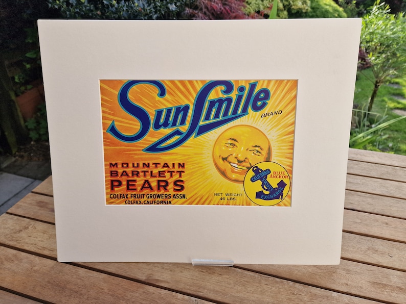 May include: Vintage Sun Smile brand label for Mountain Bartlett Pears. The label features a yellow sun with a smiling face and the text "Sun Smile" in blue lettering. The label also includes the text "Mountain Bartlett Pears", "Colfax Fruit Growers Assn.", "Colfax, California", "Net Weight 46 Lbs", and "Blue Anchor Exchange".