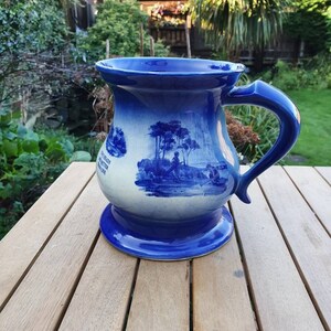 May include: A blue and white ceramic mug with a wide base and a curved handle. The mug features a gradient blue finish and a detailed blue landscape illustration. The text "TWO HEADS ARE BETTER THAN ONE" is printed on the side of the mug.