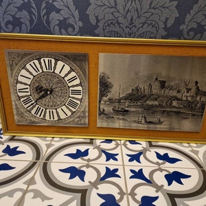 May include: A framed artwork with a gold frame and a beige mount. The artwork features two images. The left image is a clock face with Roman numerals. The right image is a black and white engraving of a castle.