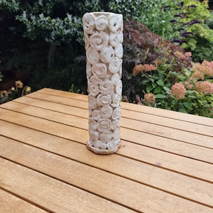 Puede incluir: Jarrón de cerámica blanco con una superficie texturizada de círculos y espirales en relieve. El jarrón está sobre una mesa de madera.